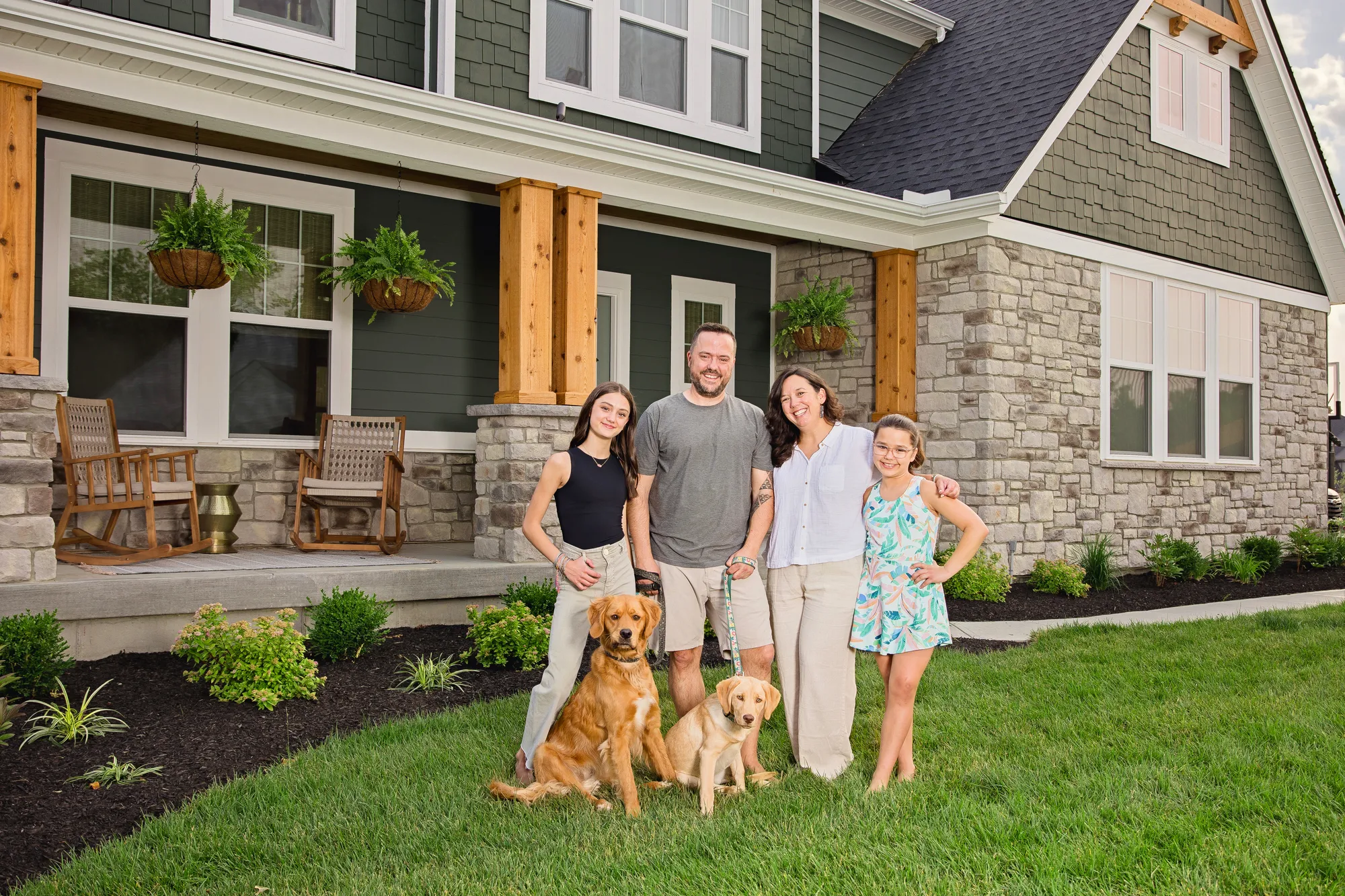 Happy family with their golden retrievers in front of their beautiful new home
